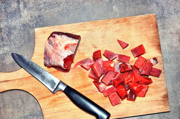 Raw red meat on a cutting board.Cuttings of red meat on a wooden board, black metal knife, on grey background
