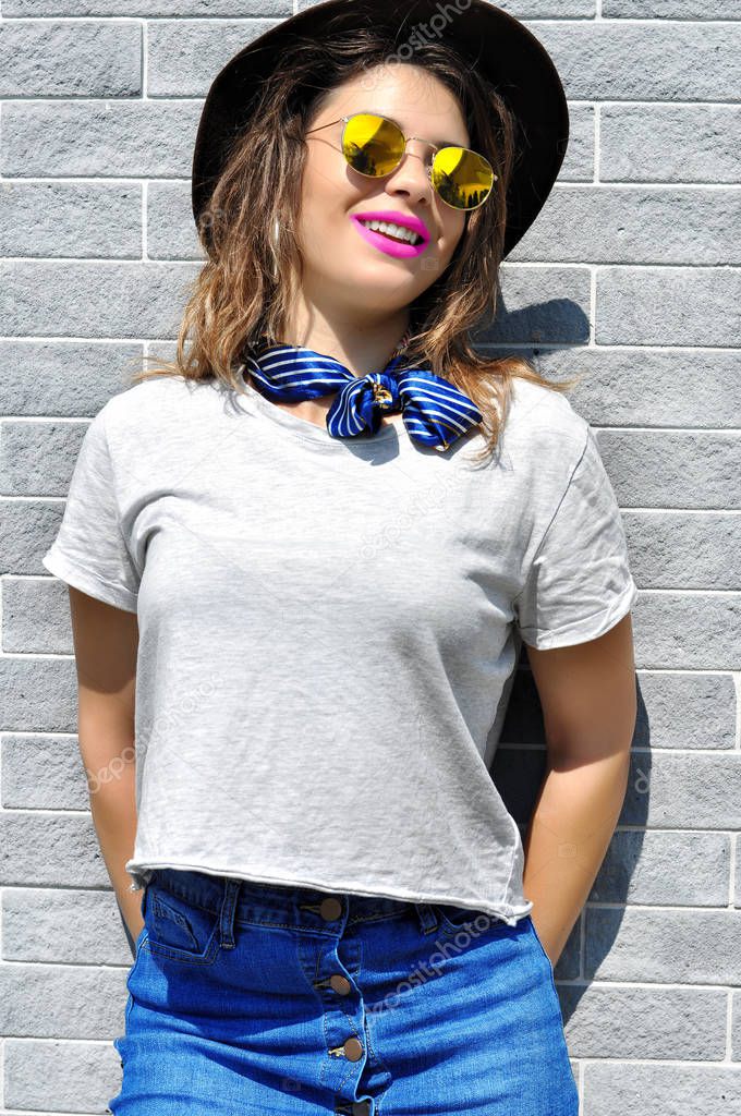 Summer city vibes. Sunny lifestyle fashion portrait pretty young smiling woman wearing trendy outfit sunglasses pink lipstick over grey background  