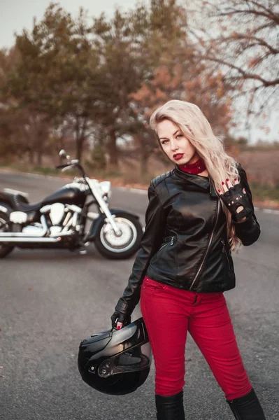Stylish biker woman with motorcycle on the road.