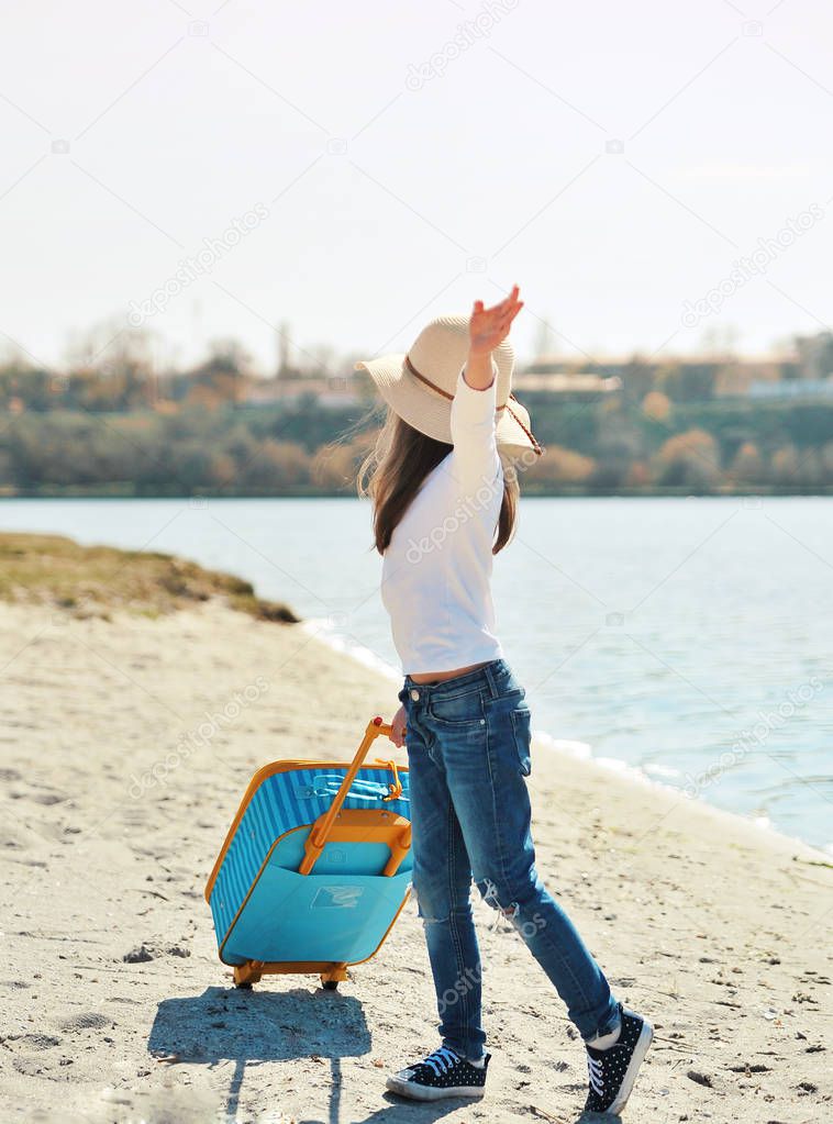 Cute little girl in hat with suitcase on the beach. Summertime concept.