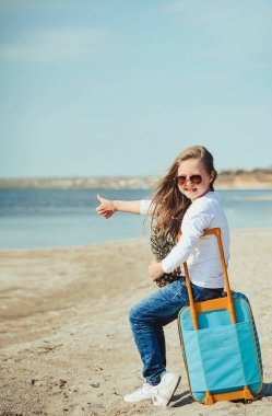 Sahilde süit çantası olan sevimli küçük kız. Yaz konsepti.