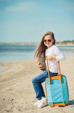 Sahilde süit çantası olan sevimli küçük kız. Yaz konsepti.
