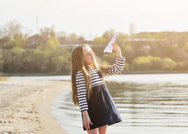 Sevimli küçük kız plajda kağıt uçak ile oynuyor.