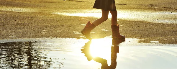 Little girl in rubber shoes jumping in autumn puddle. Happy childhood concept.