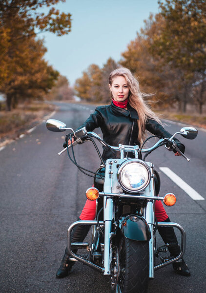 Stylish biker woman with motorcycle on the road.