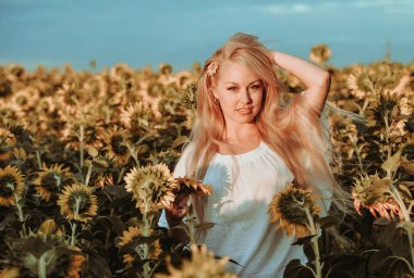 Beyaz elbiseli güzel beyaz kadın çayırda ayçiçekleriyle poz veriyor..