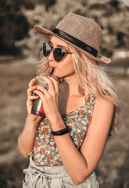 Beautiful young woman in stylish hat with summer cold drink has a fun outdoors.