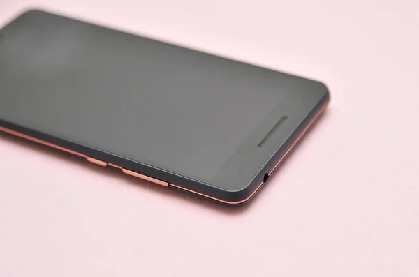 Black mobile phone on pink background.