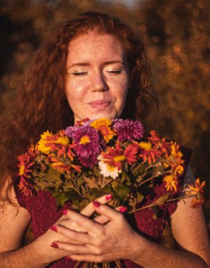 Açık havada elinde çiçekler ile Kızıl saçlı kadın.
