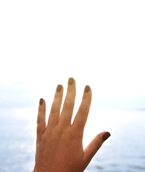 Female hand with black nails on sky background.