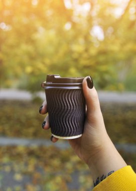 Sonbahar arka planında kahve fincanı olan bir kadın eli..