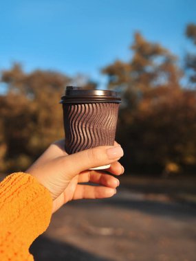 Sonbahar arka planında kahverengi kahve fincanı olan bir kadın eli..