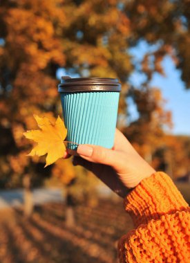 Sonbahar arka planında mavi kağıt kahve fincanı olan bir kadın el..