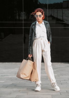 Deri ceketli şık bir kadın dışarıda poz veriyor.