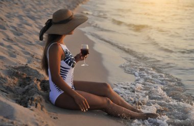  Yaz zamanı. Büyük şapkalı kadın, gün batımı kumsalında cam domuzlu..