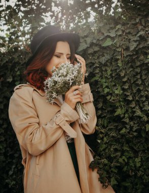 Dışarıda çiçeklerle poz veren şapkalı güzel bir kadın..