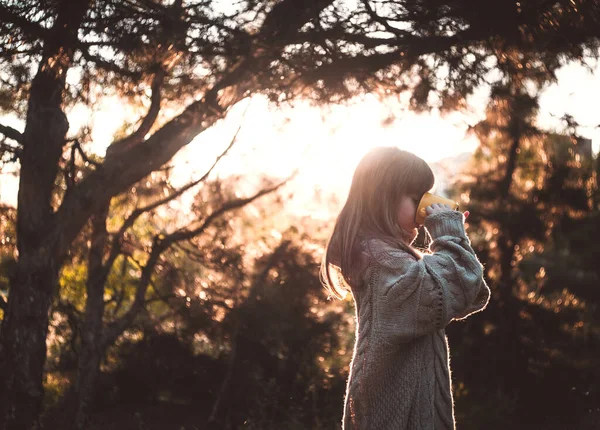 Süveter giyen şirin küçük kız ormanda sıcak çay içiyor..