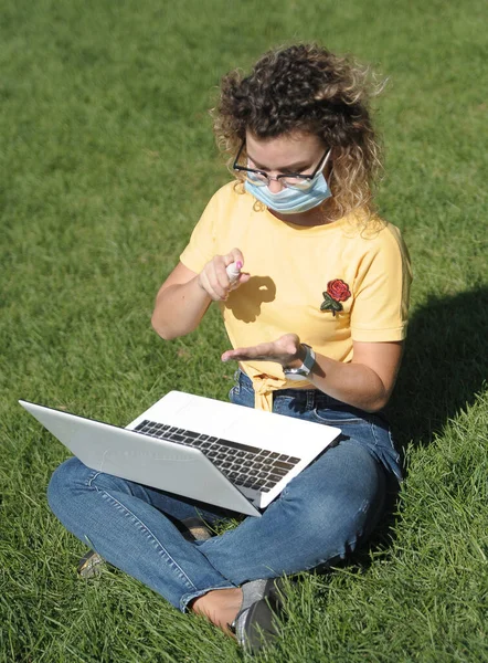 Young woman in mask on distance education works with laptop. Online education, Student sanitizers hands .