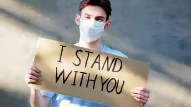 Elinde karton bir poster olan maskeli bir adam ve üzerinde yazı var. Seninle birlikteyim. Bir protesto