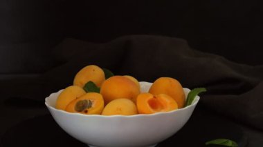 Taze kayısılar. Koyu arkaplanda kayısısı olan bir tabak. Kadın kayısı yarımlarını tabağa koyar.