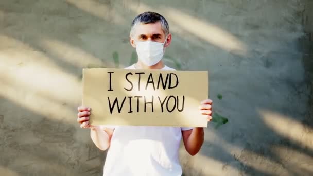 碑文と彼の手の中に段ボールのポスターとマスクの白髪の男 私はあなたと一緒に立っています 抗議の一つ — ストック動画
