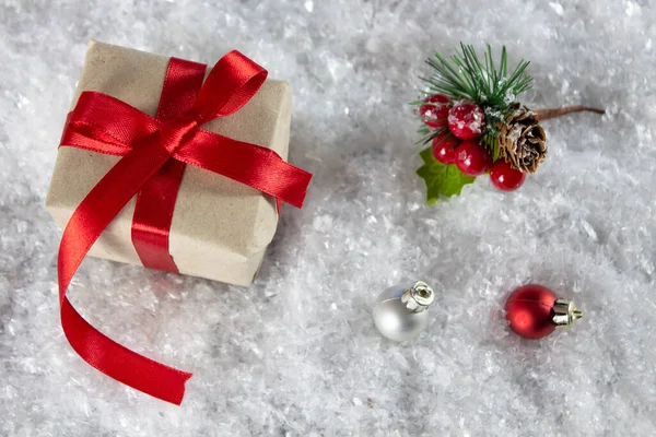 Karda kırmızı fiyonklu Noel hediyesi kutusu. Noel ağacı oyuncağı ve kırmızı böğürtlenli ladin dalı. Yukarıdan bak. Kopyalama alanı