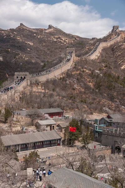 2010 Badaling で万里の長城壁上部と底辺の村の人々 Walkling でダウン フロントまで赤い中国の旗と 青い空の下の地平線上の山 — ストック写真