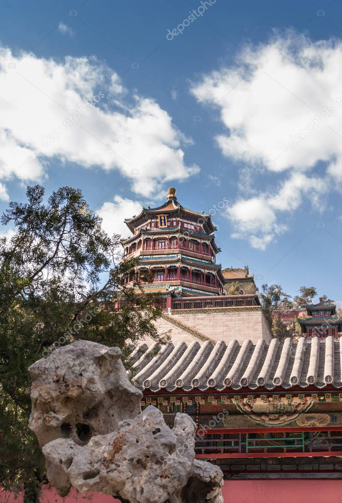 Beijing, China - April 29, 2010: Summer Palace. The pagoda towers over smaller buildings with gray roofs in rock garden under blue sky with white clouds