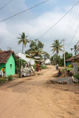 Naralapura, Karnataka, Hindistan - 1 Kasım 2013: Ana kahverengi toprak yolda birkaç evleriyle köyü önlerinde çocuklu kadınlar görüntüleyin. Yeşil ağaçlar, mavi gökyüzü beyaz bulutlar ile.