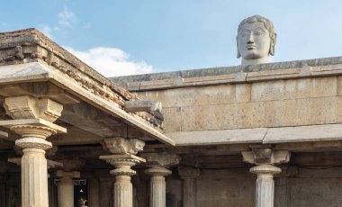 Shravanabelagola, Karnataka, Hindistan - 1 Kasım 2013: At Jain Tirth gri granit dev Bhagwan Bahubali kafa kahverengi taş tapınak ışık mavi gökyüzü karşı bina yukarıda koyar.