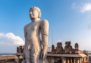 Shravanabelagola, Karnataka, Hindistan - 1 Kasım 2013: Jain Tirth günbatımında granit dev Bhagwan Bahubali heykel gri. Whie bulut ile mavi gökyüzü. Fon olarak bina kahverengi taş Tapınak