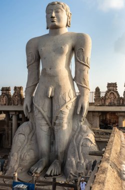 Shravanabelagola, Karnataka, Hindistan - 1 Kasım 2013: Jain Tirth granit dev Bhagwan Bahubali heykel gri. Tapınak inşa ve gökyüzü arka tarafta. Gün batımı karanlık gökyüzü. taraftan ateş, fotoğrafta rahip.