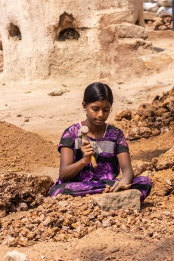 Hunsur, Karnataka, Hindistan - 1 Kasım 2013: Oturan genç kız ağır çekiç ile kireçtaşı dövüyor. Onun tarafında taş yığını. Fırın arka parçası.
