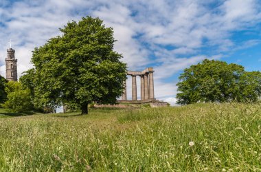 Edinburgh, İskoçya, İngiltere - 13 Haziran 2012: Nelson ve Calton Hill arasında yeşil ağaçların arkasında yeşil çim ve mavi bulutlu gökyüzü altında yakalanan Milli zafer anıtları.