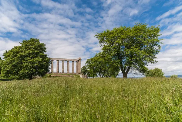 エジンバラ スコットランド イギリス 2012 国立記念碑は白い雲と青い空を背景に茶色の Pilars のシリーズです 緑の草はフロントまで つのツリー — ストック写真