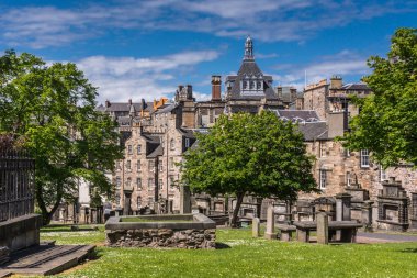 Edinburgh, İskoçya, İngiltere - 13 Haziran 2012: Mezarlık Greyfriars churk veya mavi gökyüzü altında yeşil çim, ağaçlar ve mezar taşları ile kirk. Merkez kule Kütüphane ile kahverengi taş konut zemin olduğunu.