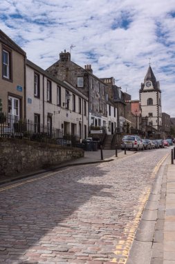 Queensferry, İskoçya, İngiltere - 14 Haziran 2012: High Street üzerinde evlerin sessiz satır farklı renk cepheler gelen. Gri yol yüzeyi ve cennet. Jubilee Saat Kulesi sonunda. Park edilmiş arabalar.