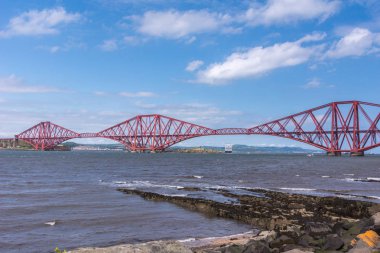 Queensferry, İskoçya, İngiltere - 14 Haziran 2012: Kırmızı portre metal ikonik Forth köprü mavi gökyüzü ve masmavi bir deniz arasında Firth of Forth üzerinden tren için.