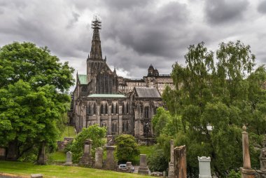 Glasgow, İskoçya, İngiltere - 17 Haziran 2012: Katedrali çok üstte yeşil çatılar ve koyu kahverengi spire iskele ile bina mezarlık görüldü. ağır cennet. Mezar taşları ve yeşil yaprakları.