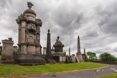 Glasgow, İskoçya, İngiltere - 17 Haziran 2012: Nekropolis. John Henry Alexander, kahverengi taş anıtsal Türbesi karşı ağır gökyüzü heykel ile. Yeşil çim. Diğer mezar anıtları çevresinde.
