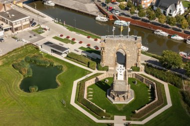 Diksmuide, Flanders, Belçika - 15 Eylül 2018: Havadan görünümü Pax kapısı ve crypt harabe arkada Ijzertoren düz Ijzer Nehri ile üzerinde. Beyaz haç, yeşil çim, bina ve karanlık su gemilerde AVV-Vvk sembolü. Ijzertoren tepesinden vurdu.