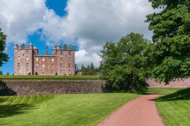 Holm Drumlanrig, İskoçya, İngiltere - 18 Haziran 2012: uzun atış serbest duran pembe kum taş Castle Drumlanrig bulutlu gökyüzü altında tarafına driveway boyunca. Yemyeşil ağaçlar ve çimenler.