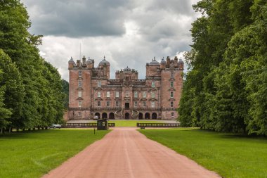 Holm Drumlanrig, İskoçya, İngiltere - 18 Haziran 2012: atış serbest duran driveway boyunca pembe kum taş Castle Drumlanrig bulutlu gökyüzü altında. Her iki tarafta yeşil ağaçlar duvarına.
