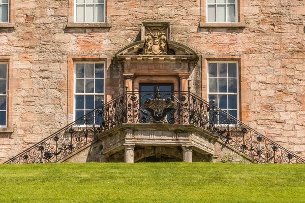 Holm of Drumlanrig, Scotland, UK - June 18, 2012: Back door with double staircase at garden side of free standing pink sand stone Drumlanrig Castle on its higher plateau. Green lawn up front.