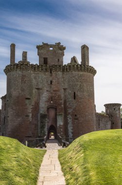 Shearington, İskoçya, İngiltere - 18 Haziran 2012: Yıkık üçgen kahverengi taş için yol Caerlavarock kale mavi gökyüzü altında moated ve yeşil çim ve orman arkada ayarla.