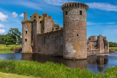Shearington, İskoçya, İngiltere - 18 Haziran 2012: Batı ve Güney tarafı yıkık üçgen kahverengi taş Caerlavarock kale mavi gökyüzü altında moated ve hendek tarafından çevrili.