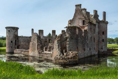 Shearington, İskoçya, İngiltere - 18 Haziran 2012: Güney ve Doğu tarafı yıkık üçgen kahverengi taş Castle Caerlavarock moated. Hendek ve köşe kule.