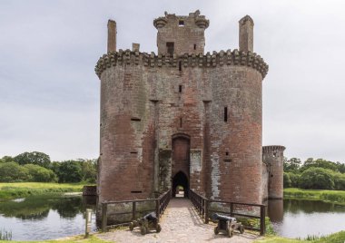 Shearington, İskoçya, İngiltere - 18 Haziran 2012: Giriş Kulesi yıkık üçgen kahverengi taş Castle Caerlavarock gümüş mavi gökyüzü moated. Hendek ve topları ile Köprü. Horizon olarak yeşil kuşak.