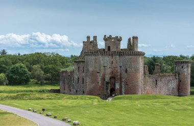 Shearington, İskoçya, İngiltere - 18 Haziran 2012: Yıkık üçgen kahverengi taş Castle Caerlavarock mavi gökyüzü altında moated. Artık bu yeşil çim ve yeşil orman kemer horizon olarak gösterilen vurdu.