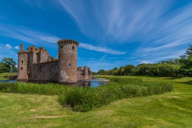 Shearington, İskoçya, İngiltere - 18 Haziran 2012: Güneybatı Kulesi ve harap kahverengi taş Castle Caerlavarock mavi gökyüzü altında iki duvar çok uzun atış. Geniş hendek, yeşil çim ve ağaçların.